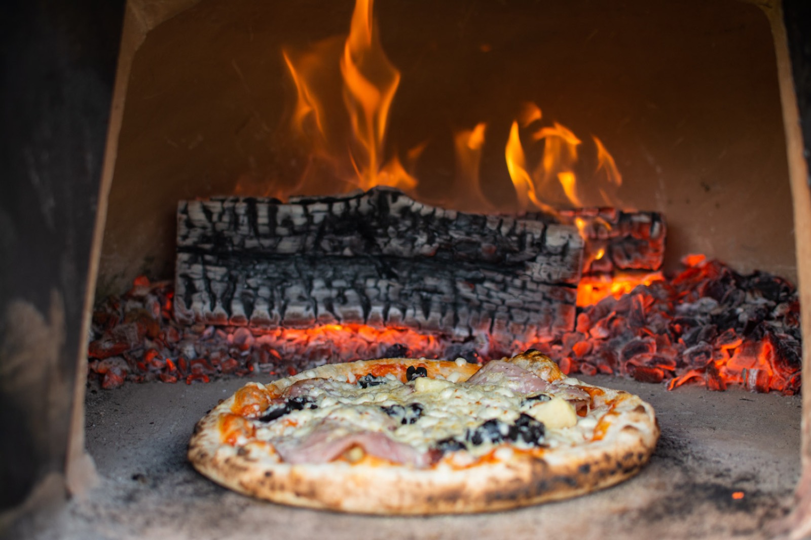 Pizza in de houtoven van Carciofo, met vlammen op de achtergrond